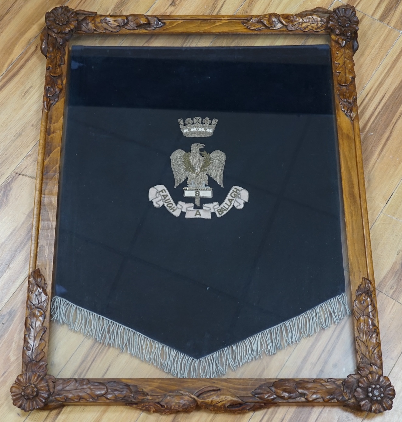 A framed bandsman’s banner of the Royal Irish Fusiliers, a crowned eagle in silver thread, over ‘8 Faugh A Ballagh’, 64 x 52cm, in a carved oak frame. Condition - good.